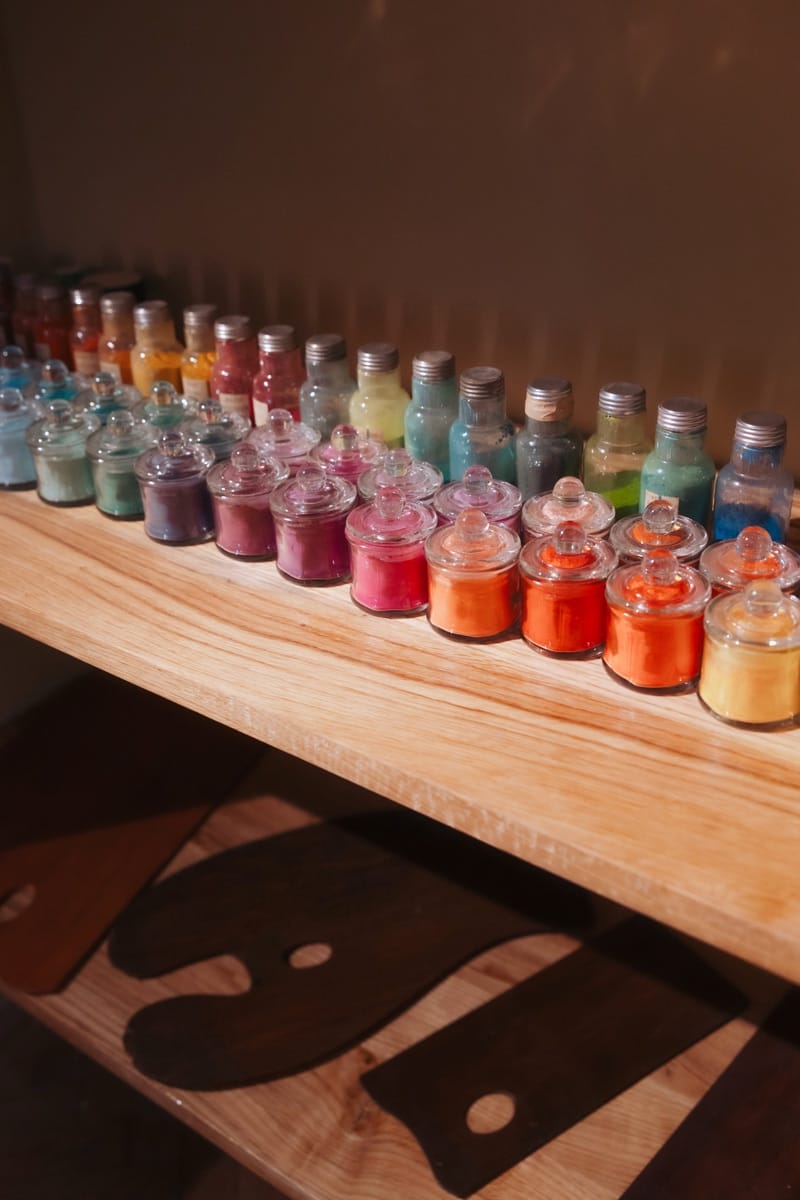 Row of period pigment jars displayed on a wooden shelf in the exhibition